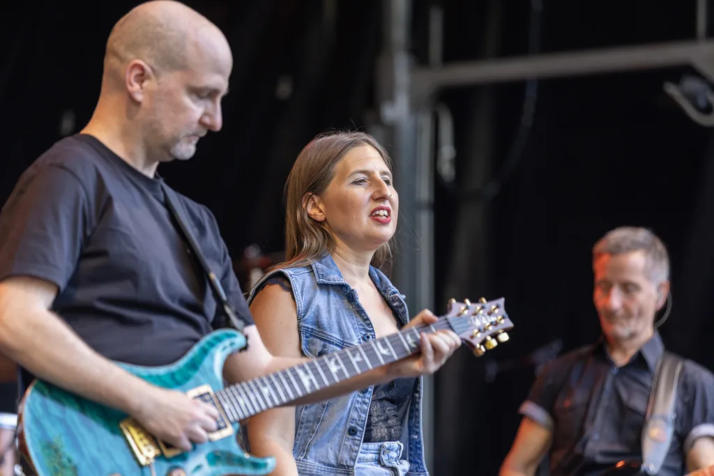 Gitarrist Alexander Stocker spielt neben Sängerin Maren Disch, während Bassist Jürgen Wernet im Hintergrund auf der Bühne steht.