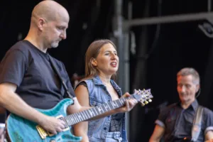 Gitarrist Alexander Stocker spielt neben Sängerin Maren Disch, während Bassist Jürgen Wernet im Hintergrund auf der Bühne steht.