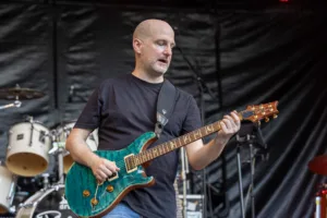 Gitarrist Alexander Stocker spielt seine grüne E-Gitarre vor Schlagzeug und schwarzem Bühnenvorhang.