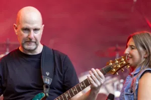 Gitarrist Alexander Stocker spielt im roten Bühnenlicht, während Sängerin Maren Disch unscharf neben ihm steht.