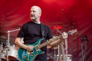 Gitarrist Alexander Stocker spielt seine grüne E-Gitarre im roten Licht und blickt über die Bühne.