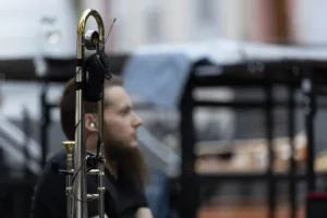 Posaunist Simon Kräuter steht hinter seinem Instrument am seitlichen Bühnenrand, während Technik und Absperrgitter den Hintergrund prägen.
