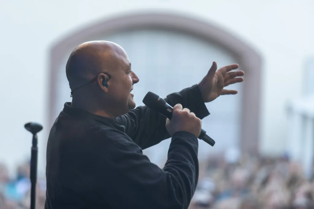 Phil It Sänger Sascha Spitz richtet sich mit Mikrofon und ausgestrecktem Arm an das Publikum vor der Open-Air-Bühne.