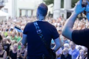 Gitarrist Sascha Happle spielt mit dem Rücken zur Kamera am Bühnenrand, während vor ihm ein großes Publikum den Platz füllt.