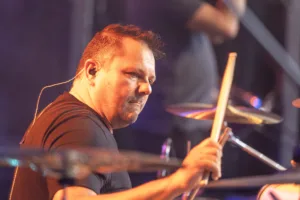 Schlagzeuger Andreas Scheerer spielt hinter den Becken, von warmem Seitenlicht beleuchtet und mit erhobenem Drumstick im Anschlag.