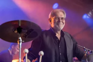 Percussionist Michael Scherer steht lächelnd hinter einem großen Becken, umgeben von violettem Licht und leichtem Bühnennebel.