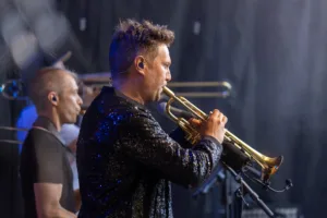 Trompeter Dennis Frommherz spielt im Vordergrund, während Saxofonist Max Marlier und weitere Bläser gestaffelt hinter ihm stehen.