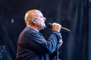 Sänger Sascha Spitz singt im Profil in sein Handmikrofon, vor einem dunklen Bühnenhintergrund mit vereinzelten Lichtpunkten.