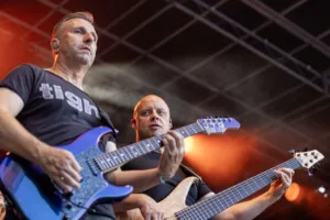 Gitarrist Sascha Happle und Bassist Steffen Vogt spielen nebeneinander unter orangefarbenem Bühnenlicht und dem offenen Bühnendach.