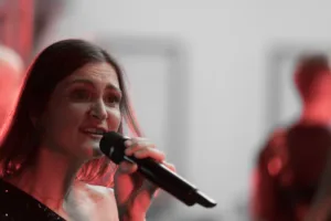 Sängerin Tamara Hoppe singt ins Handmikrofon, während rotes Licht ihr Gesicht und den hellen Hintergrund akzentuiert.