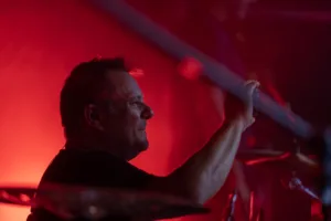 Schlagzeuger Andreas Scheerer sitzt als dunkle Silhouette hinter seinem Drumset, umgeben von intensiv rotem Bühnenlicht.