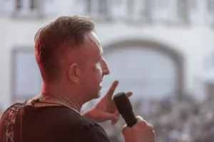 Gitarrist Sascha Happle steht mit Mikrofon vor dem großen Publikum und gestikuliert mit der freien Hand vom Bühnenrand aus.