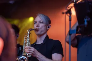 Saxofonist Max Marlier spielt unter orangefarbenen und grünen Scheinwerfern, während Mikrofone über seinem Instrument hängen.