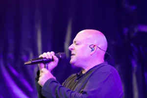 Sänger Sascha Spitz umfasst das Mikrofon mit beiden Händen und singt vor violettem Licht und dunklen Bühnenvorhängen.