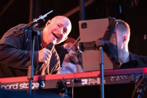 Sänger Sascha Spitz beugt sich mit dem Mikrofon über Keyboarder Tim Girons Instrument, während ein Tablet zwischen ihnen steht.