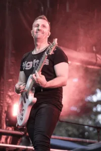 Gitarrist Sascha Happle spielt breitbeinig am Bühnenrand, während weißes Licht und Nebel die niedrige Perspektive verstärken.