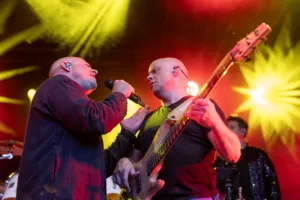 Sänger Sascha Spitz singt Bassist Steffen Vogt aus nächster Nähe zu, während gelbe und rote Strahlen hinter ihnen aufleuchten.