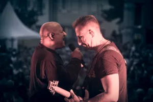 Sänger Sascha Spitz und Bassist Steffen Vogt stehen Stirn an Stirn am Bühnenrand, Mikrofon und Gitarre dicht zwischen ihnen.