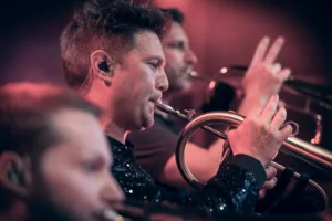 Drei Musiker des Phil-It-Bläsersatzes spielen gestaffelt hintereinander, mit einer Trompete im scharf abgebildeten Vordergrund.
