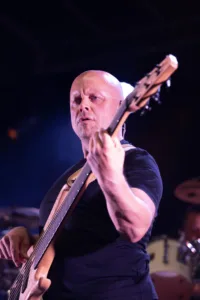 Bassist Steffen Vogt spielt aus tiefer Perspektive in die Kamera, der Basshals ragt diagonal in den violett beleuchteten Bühnenraum.