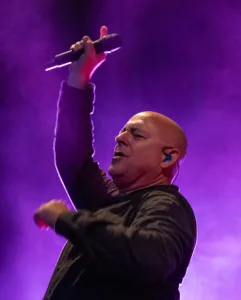 Sänger Sascha Spitz singt mit hoch erhobenem Mikrofon und ausgestrecktem Arm unter violettem Licht und Bühnennebel.