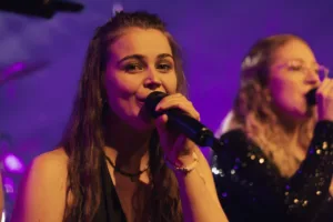 Sängerin Marleen Hoppe singt im Vordergrund ins Mikrofon, während Sängerin Jana Maier leicht versetzt hinter ihr steht.