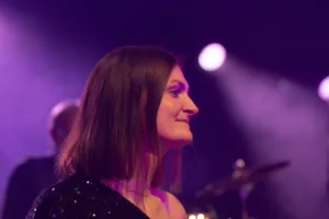Sängerin Tamara Hoppe blickt im violetten Bühnenlicht zur Seite, während Mikrofon und weitere Musiker im Hintergrund verschwimmen.