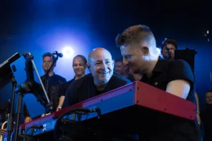 Keyboarder Tim Giron und Sänger Sascha Spitz beugen sich lächelnd über das rote Keyboard, während Bandmitglieder hinter ihnen stehen.