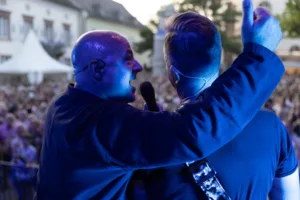 Sänger Sascha Spitz und Gitarrist Sascha Happle stehen mit dem Rücken zur Kamera vor dem Publikum, ein Arm weist über den Platz.