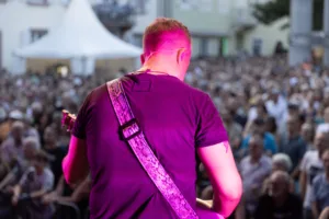 Gitarrist Sascha Happle spielt mit dem Rücken zur Kamera am Bühnenrand, während das dicht stehende Publikum direkt vor ihm zusieht.