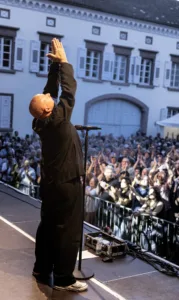 Sänger Sascha Spitz steht vor dem Publikum und hebt beide Hände über den Kopf, gesehen von der Rückseite der Open-Air-Bühne.