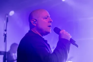 Sänger Sascha Spitz singt im Profil ins Handmikrofon, während violettes Licht und Bühnennebel die Konturen seines Gesichts betonen.