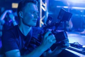 Der Kameramann hält seine professionelle Filmkamera auf Schulterhöhe und verfolgt den Auftritt im intensiven blauen Bühnenlicht.