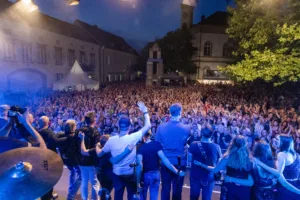 Phil It steht nach dem Auftritt gemeinsam mit dem Rücken zur Kamera vor dem großen Publikum auf dem beleuchteten Marktplatz.